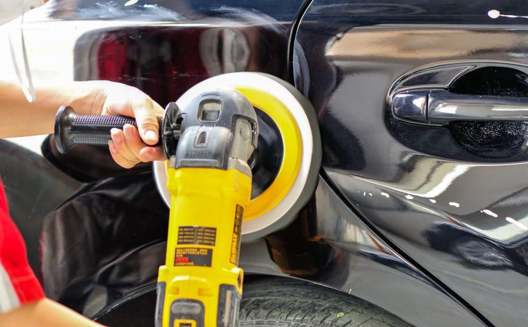 A skilled technician performing paintless dent removal with a yellow tool on a shiny black car.